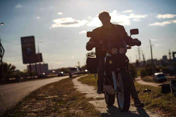 Close-up vista sobre o motociclista de pé perto da motocicleta em uma estrada vazia no dia ensolarado — Fotografia de Stock
