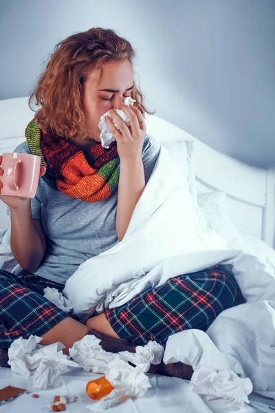 Άρρωστο κορίτσι στο μαντήλι κάθεται στο κρεβάτι και να φυσάει τη μύτη της — Φωτογραφία Αρχείου