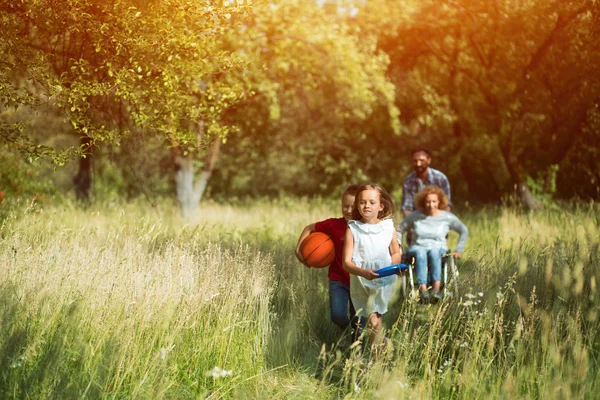 Děti běžel a smát se, zatímco jejich matky na vozíku a otec běží za nimi — Stock fotografie