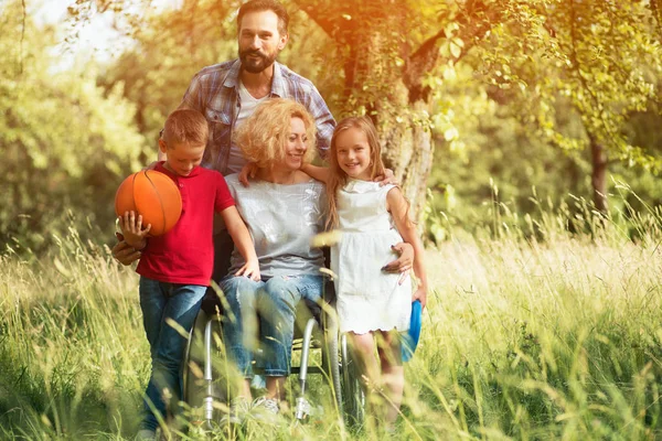 Un ritratto di famiglia. Donna su una sedia a rotelle con la sua famiglia all'aperto . — Foto Stock