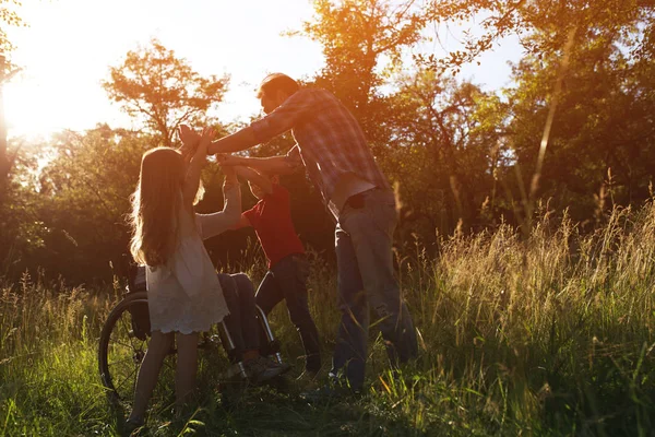 Woman in an armchair has fun with her husband and two children in park — Stock Photo, Image