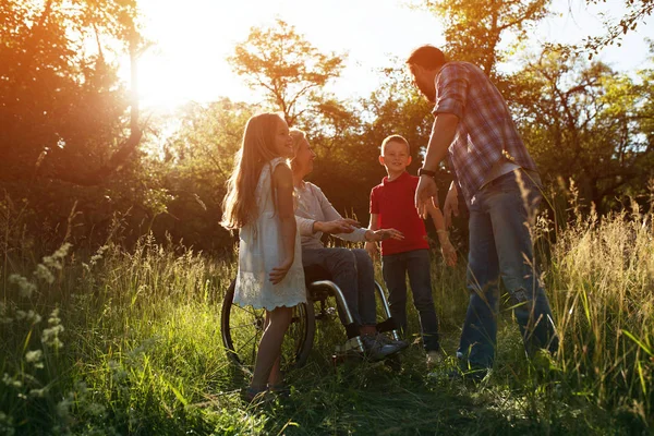 Femme dans un fauteuil s'amuse avec son mari et deux enfants dans le parc — Photo