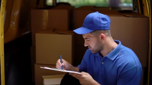 Delivery man is sitting at the back of yellow truck, filling documents — Stock Video