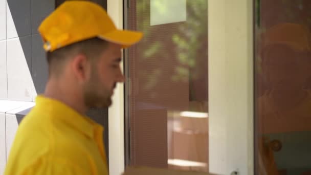 Correio em uniforme amarelo toca um sino e dá caixas de pizza para mulher recebendo dinheiro em troca — Vídeo de Stock