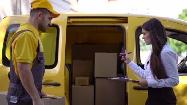 Affärskvinna kontrollerar leverans från courier i gula uniform utomhus nära hans bil — Stockvideo