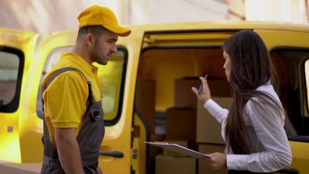 Zakenvrouw controleert levering van courier in geel uniform buiten in de buurt van zijn auto — Stockvideo