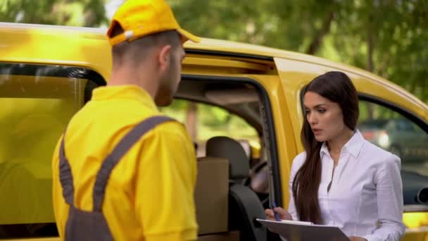 Бізнес-леді перевіряє доставку від кур'єра в жовтій формі на відкритому повітрі біля свого автомобіля — стокове відео