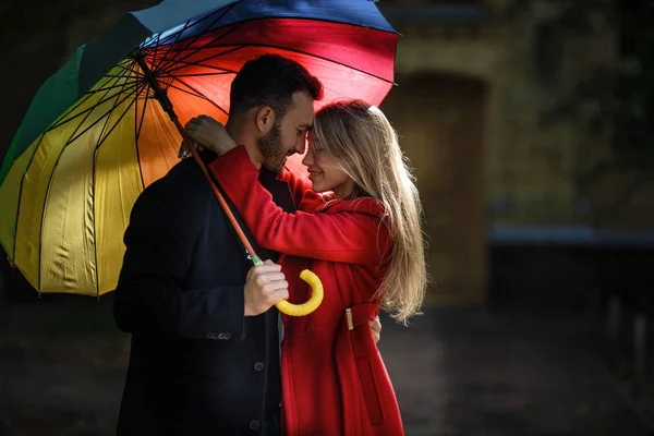 Junge Leute spazieren im Park unter buntem Regenschirm — Stockfoto