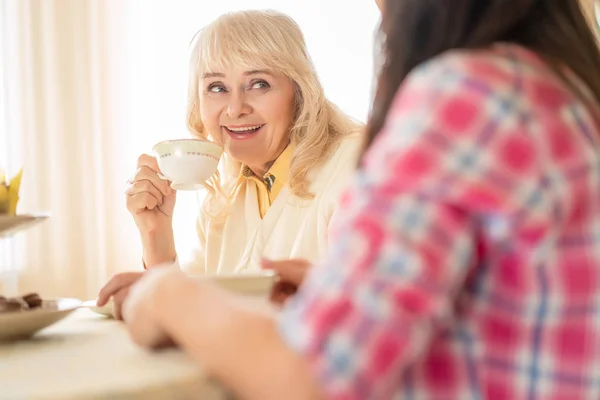 Mujer sonriente bebe té y disfruta de la conversación con una hija — Foto de Stock