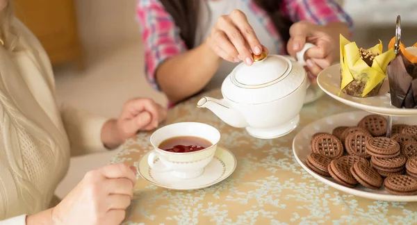 Hände einer jungen Frau mit weißer Porzellanteekanne, die Tee in die Tasse ihrer älteren Mutter gießt — Stockfoto