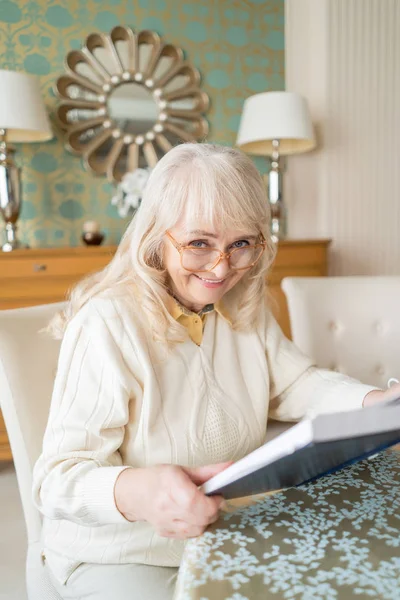 Улыбающаяся пожилая женщина читает книгу за чашкой чая — стоковое фото