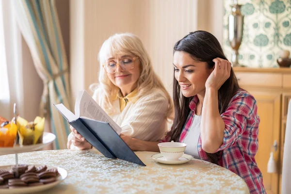 先輩母と娘はお茶を飲みながら本を読む — ストック写真