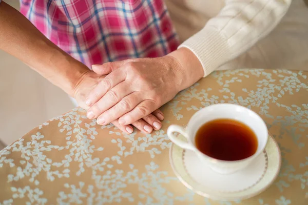 Primer plano de la mano de la madre y la hija mayores en la mesa cerca de la taza de té — Foto de Stock