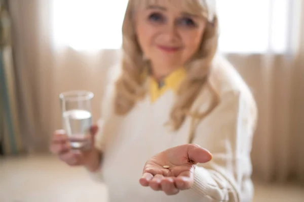 Mujer mayor sosteniendo pastillas y un vaso de agua — Foto de Stock