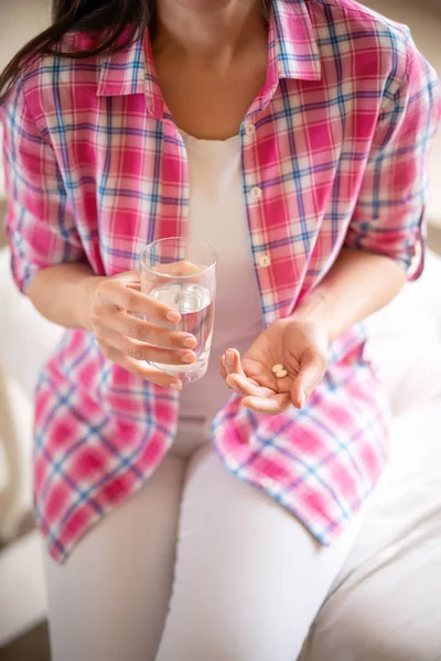 Visão superior da mulher segurando vitaminas e vidro de água sentado no sofá — Fotografia de Stock