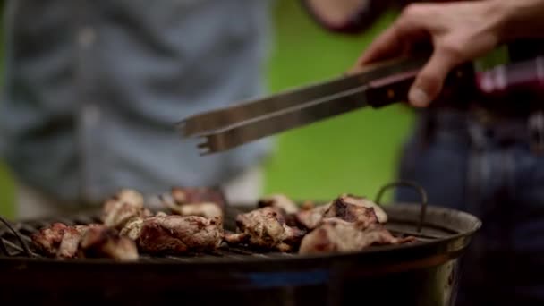Att vrida bitar av kött grillning på värme med tång. Barbecue. Närbild — Stockvideo