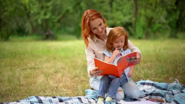 Mãe lê um livro com sua filha no parque — Vídeo de Stock
