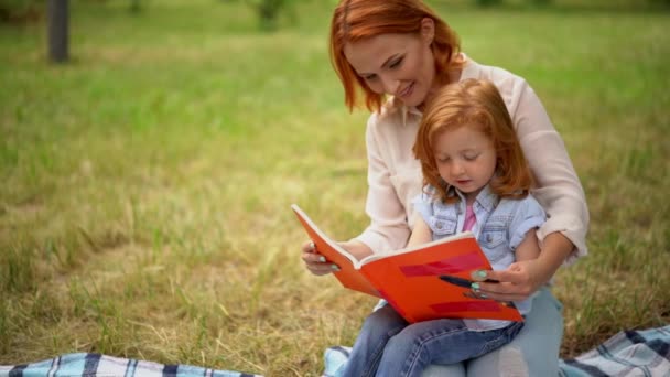 Anne ile kızını parkta bir kitap okur — Stok video