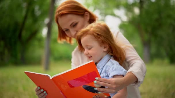 Jovem mãe feliz com sua filha lendo ao ar livre — Vídeo de Stock