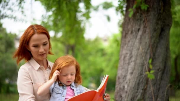 Feliz joven madre con su hija leyendo al aire libre — Vídeos de Stock