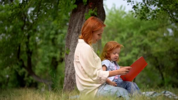 Glad ung mor med sin dotter läsa utomhus — Stockvideo