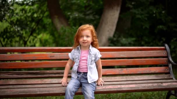 Petite fille mignonne s'assoit sur le banc — Video