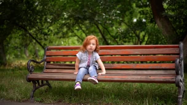 Petite fille mignonne s'assoit sur le banc — Video