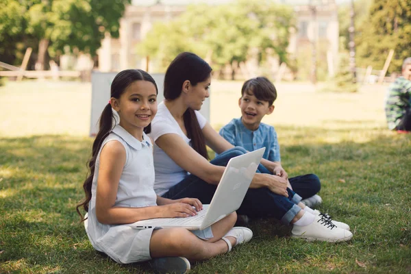 Insegnante e due giovani studenti usano il computer portatile nel parco — Foto Stock