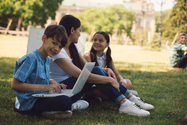 老师和两个年轻学生在公园里使用笔记本电脑 — 图库照片