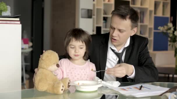 Отец в костюме работает с бумагами и кормит дочь — стоковое видео
