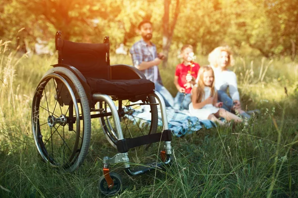 Fokus auf leeren Rollstuhl im Vordergrund, während glückliche Familie im Hintergrund ruht — Stockfoto