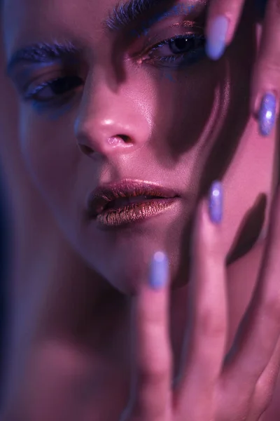 Modelo de menina elegante em tons de néon com maquiagem brilhante mantém as mãos no rosto . — Fotografia de Stock