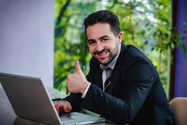 Businessman shows thumbs up sitting at the laptop