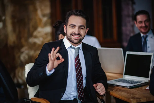 Handsome businessman shows ok gesture sitting at the table — Stock Photo, Image