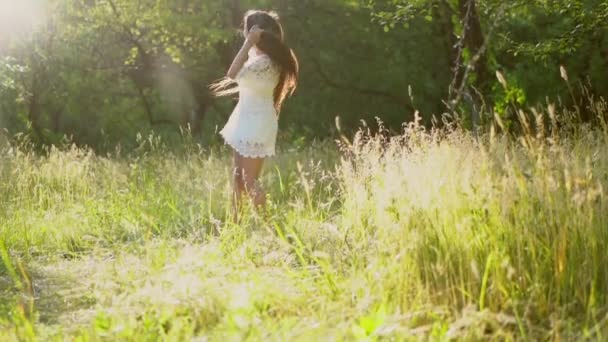 Härlig brunett flicka snurrar runt Iklädd vit klänning i parken — Stockvideo