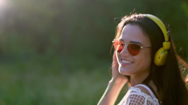 Menina em óculos de sol e grandes fones de ouvido amarelos escuta música — Vídeo de Stock