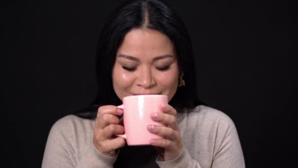 Una donna bruna su sfondo nero sta bevendo caffè con una tazza rosa . — Video Stock