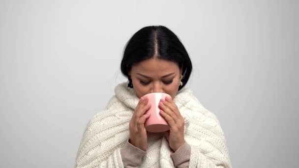 Азіатський жінка з милою посмішкою, загорнуті в теплий шарф трикотажні, пити чаї з рожевими Кубок. — стокове відео