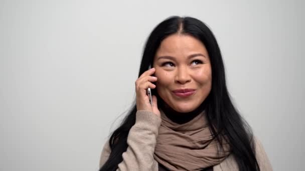 Vacker asiatisk kvinna på en vit bakgrund talar i telefon. — Stockvideo