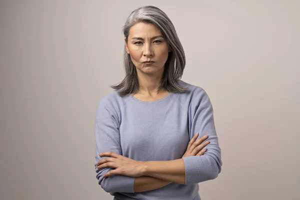 Ernsthafte mongolische Frau mit grauen Haaren vor grauem Hintergrund. — Stockfoto