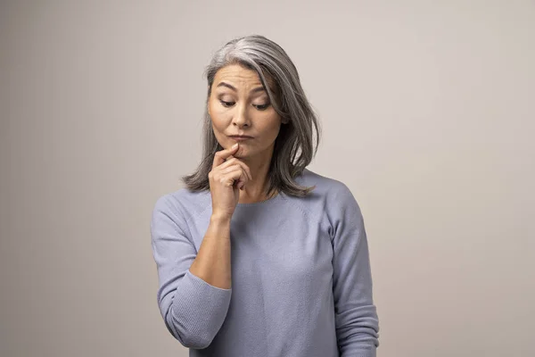 Nadenkend vrouw van de Mongoolse verschijning met grijze haren op een witte achtergrond. — Stockfoto