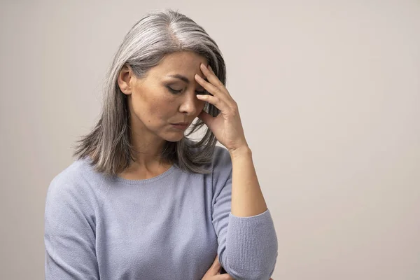 Mature Asian woman touches her forehead in distress — Stock Photo, Image