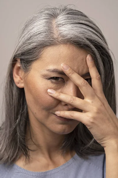 Triste femme mongole aux cheveux gris sur fond gris . — Photo