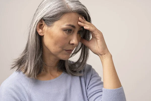 Mature Asian woman touches her forehead in distress — Stock Photo, Image