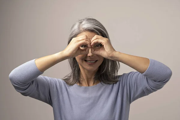 Reife mongolische Frau hält Hände, als schaue sie durch ein Fernglas. — Stockfoto