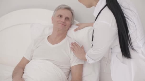 Charmanter Arzt kümmert sich um behinderten Senioren im Bett — Stockvideo