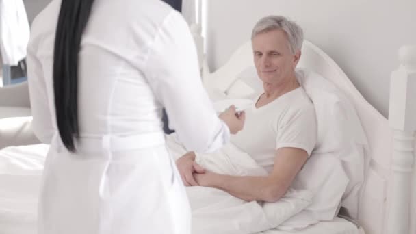 Очаровательный доктор ухаживает за инвалидом в постели. — стоковое видео