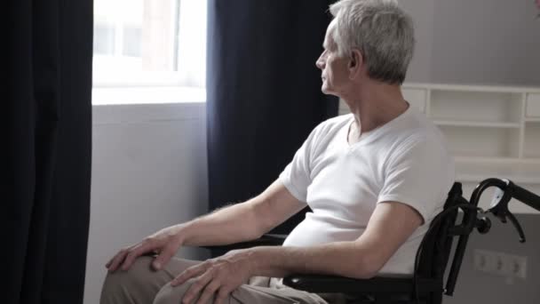 Homme aîné paraplégique en fauteuil roulant près de la fenêtre — Video