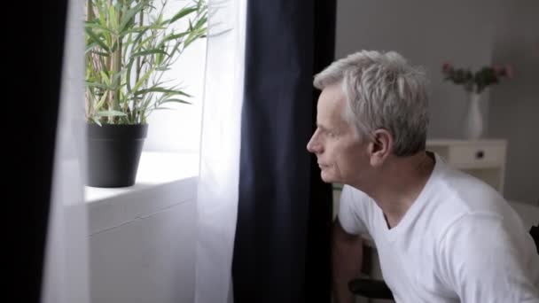 Ein älterer Mann mit grauen Haaren im Kinderwagen auf der Station gießt Blumen. — Stockvideo