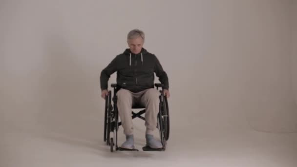 Un uomo dai capelli grigi su una sedia a rotelle con uno sguardo malvagio su uno sfondo bianco . — Video Stock